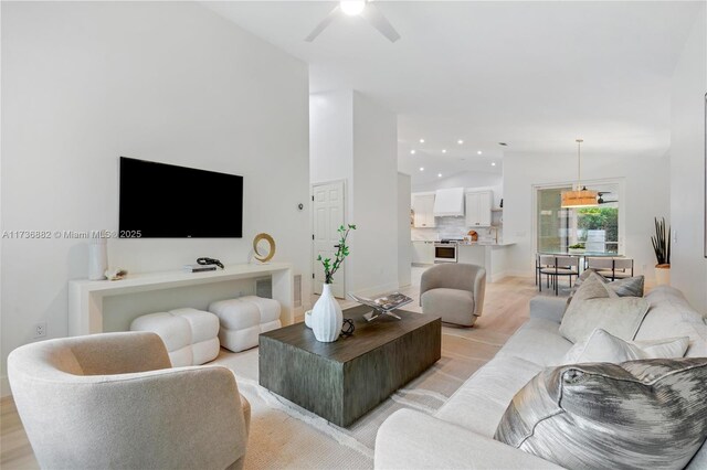 living room with lofted ceiling, ceiling fan, and light wood-type flooring