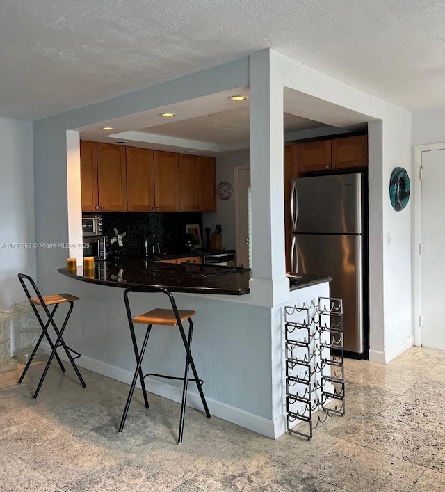 kitchen featuring a breakfast bar, backsplash, kitchen peninsula, stainless steel appliances, and a textured ceiling