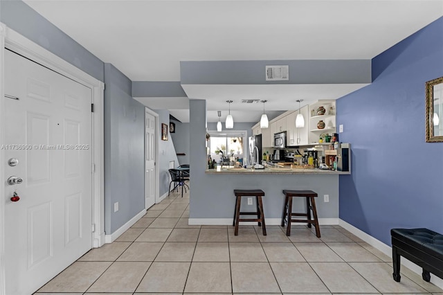 kitchen with pendant lighting, a breakfast bar area, appliances with stainless steel finishes, light tile patterned flooring, and kitchen peninsula