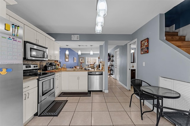 kitchen with hanging light fixtures, light tile patterned floors, kitchen peninsula, stainless steel appliances, and white cabinets