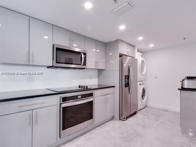 kitchen featuring gray cabinetry, appliances with stainless steel finishes, and stacked washer and clothes dryer