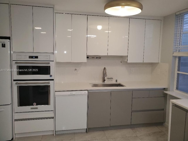 kitchen with tasteful backsplash, sink, white cabinets, light tile patterned floors, and white appliances