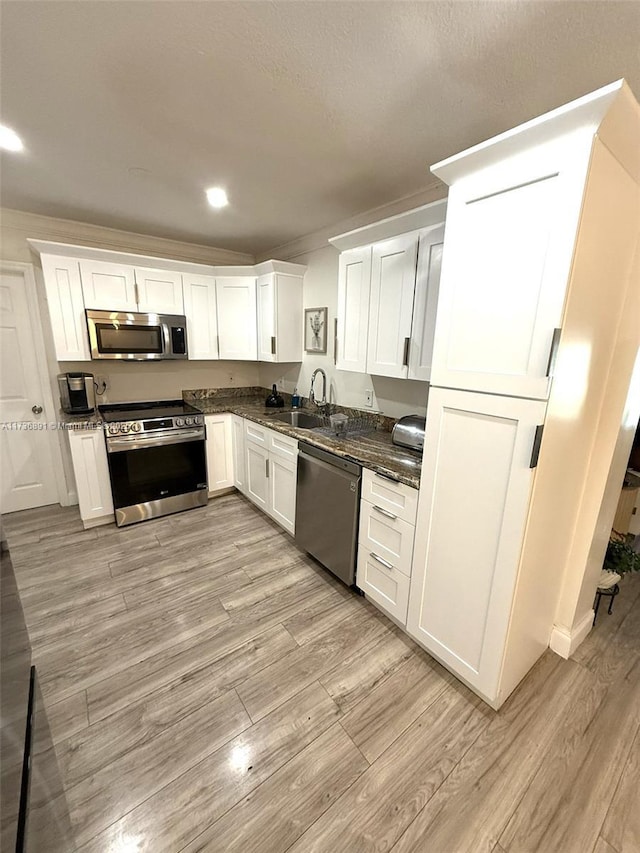 kitchen with appliances with stainless steel finishes, white cabinetry, sink, dark stone counters, and light wood-type flooring