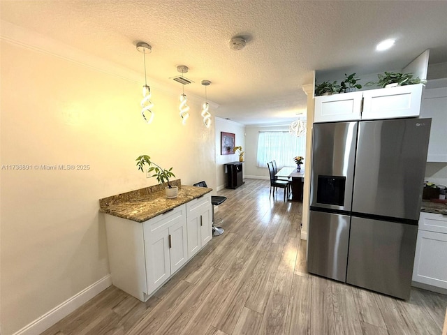 kitchen with hanging light fixtures, stainless steel refrigerator with ice dispenser, dark stone countertops, and white cabinets