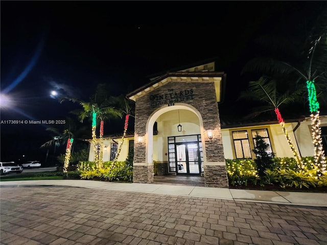 exterior entry at night with stone siding, french doors, and stucco siding