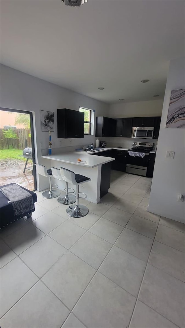 kitchen with a breakfast bar area, light tile patterned floors, stainless steel appliances, light countertops, and dark cabinets