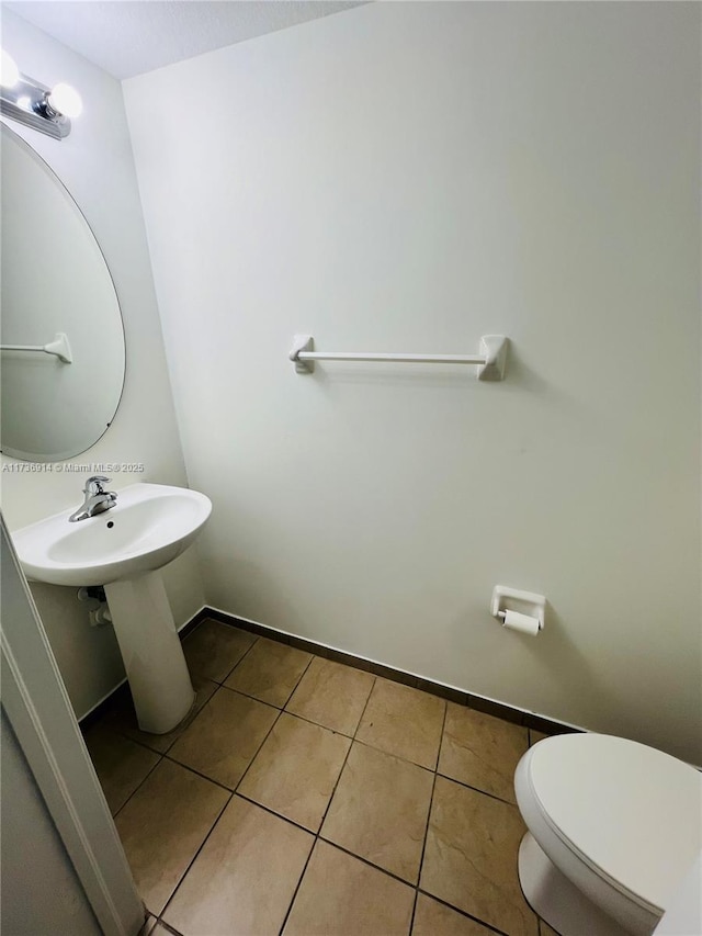 half bathroom with toilet, tile patterned flooring, and baseboards