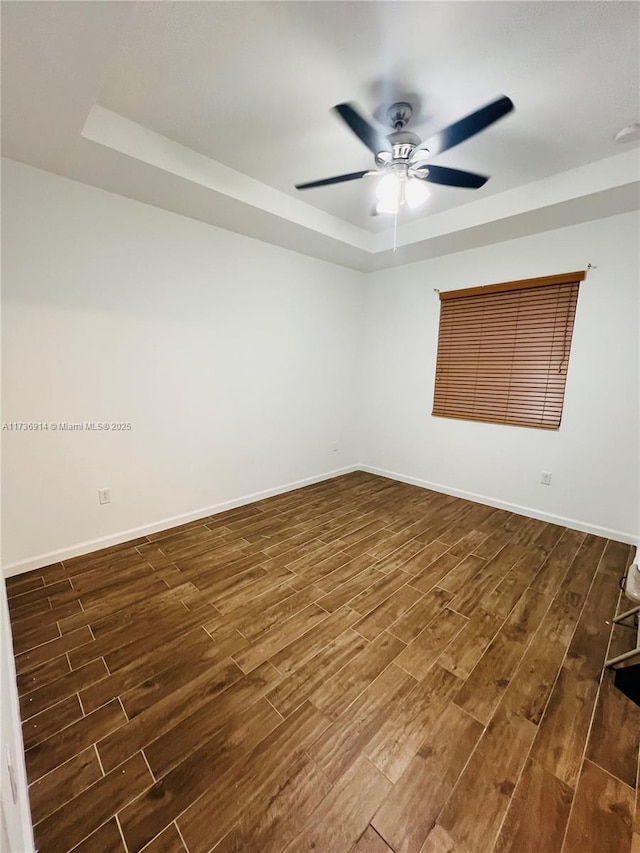 unfurnished room featuring a tray ceiling, dark wood-style flooring, ceiling fan, and baseboards