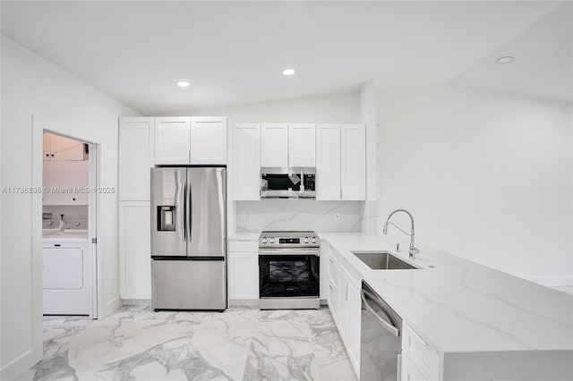 kitchen with light stone counters, appliances with stainless steel finishes, vaulted ceiling, a sink, and washer / dryer