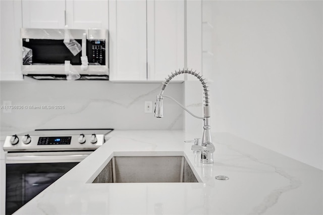 kitchen featuring stainless steel appliances, white cabinets, a sink, and light stone counters