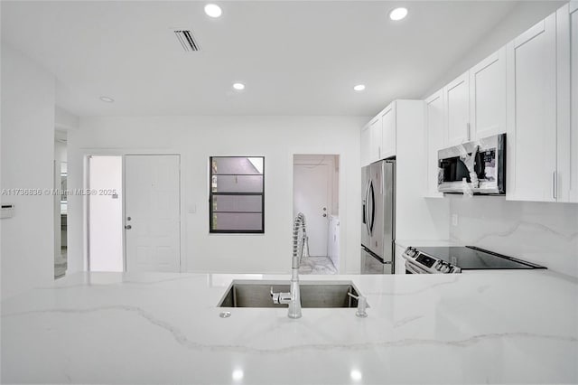 kitchen with appliances with stainless steel finishes, a sink, white cabinetry, and light stone countertops