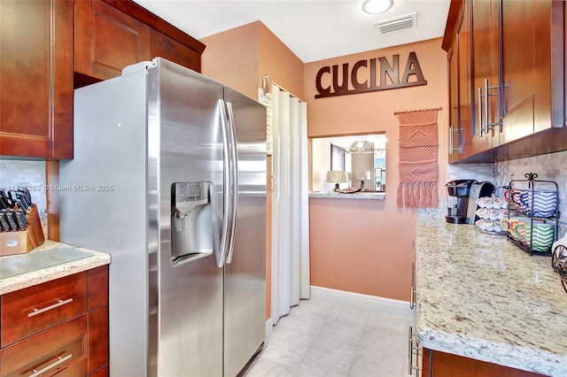 kitchen with light stone counters, decorative backsplash, and stainless steel fridge