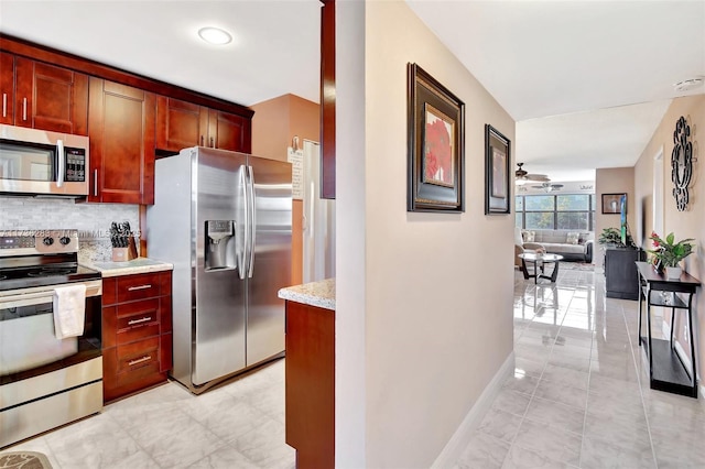 kitchen with light stone counters, ceiling fan, stainless steel appliances, and backsplash