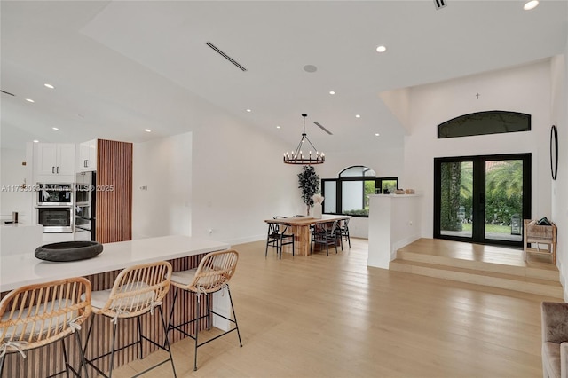 kitchen with pendant lighting, white cabinetry, stainless steel fridge, a kitchen breakfast bar, and light hardwood / wood-style floors