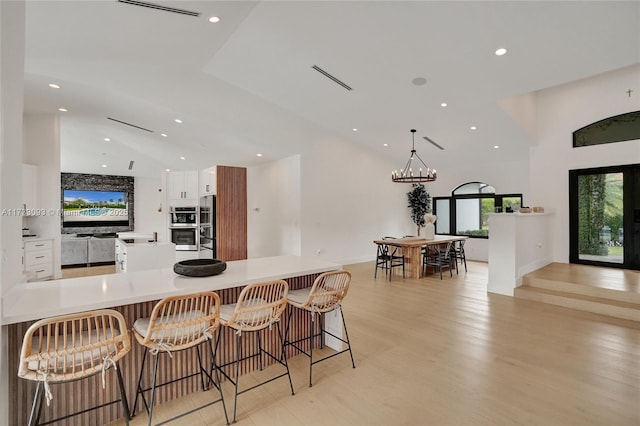 kitchen featuring a breakfast bar, stainless steel appliances, light hardwood / wood-style floors, white cabinets, and decorative light fixtures