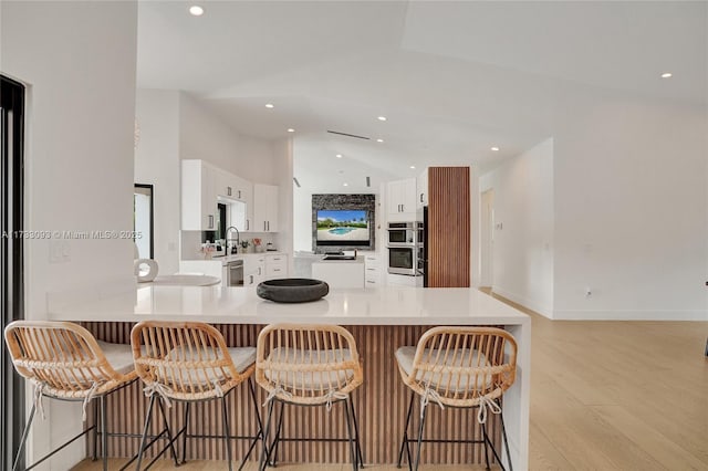 kitchen featuring lofted ceiling, a breakfast bar, light hardwood / wood-style flooring, kitchen peninsula, and white cabinets