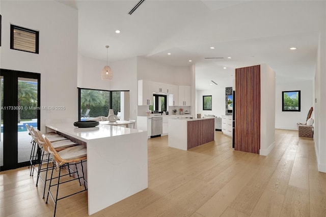 kitchen with decorative light fixtures, white cabinetry, dishwasher, a breakfast bar area, and a high ceiling