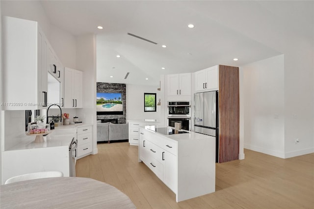 kitchen featuring white cabinetry, lofted ceiling, a center island, stainless steel appliances, and light wood-type flooring