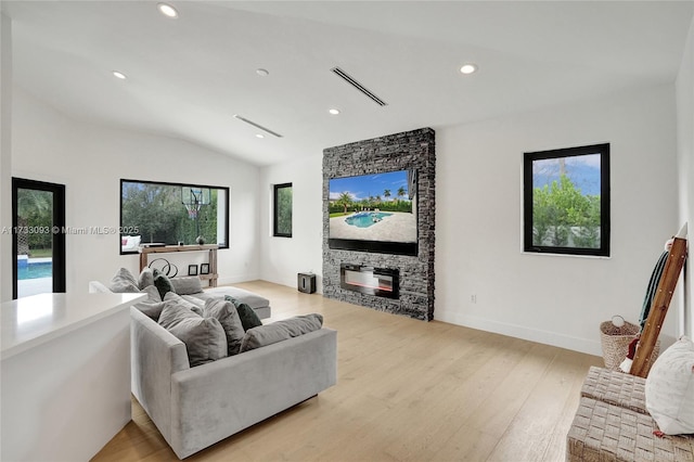 living room featuring lofted ceiling, a stone fireplace, a wealth of natural light, and light wood-type flooring