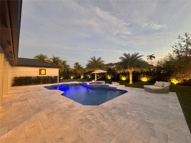 pool at dusk with a patio area and an in ground hot tub