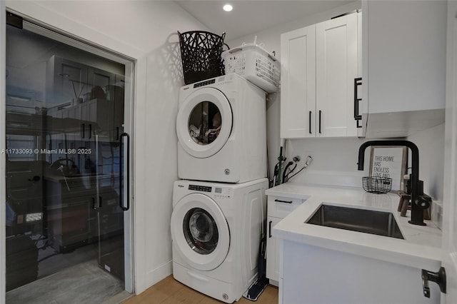 clothes washing area with cabinets, stacked washer and clothes dryer, sink, and light hardwood / wood-style flooring