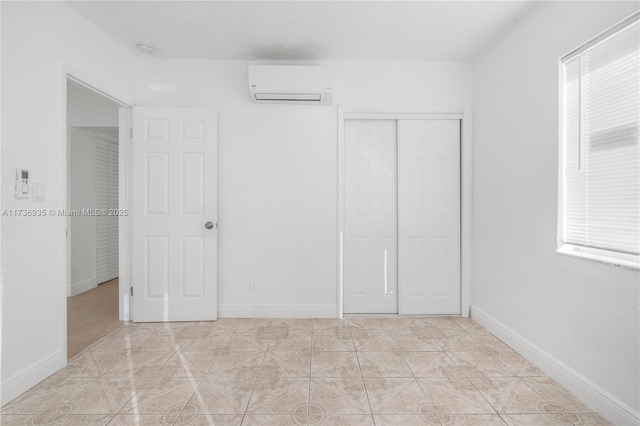 unfurnished bedroom with an AC wall unit, light tile patterned floors, and a closet