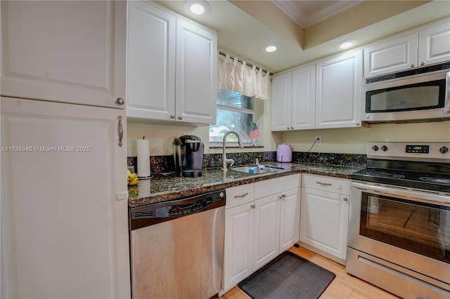 kitchen with sink, appliances with stainless steel finishes, white cabinets, dark stone counters, and light wood-type flooring