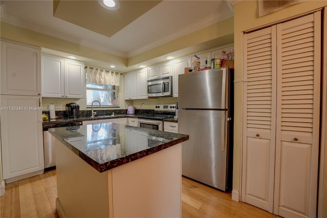 kitchen with white cabinetry, stainless steel appliances, a center island, dark stone counters, and light wood-type flooring