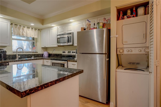 kitchen with stacked washer and clothes dryer, crown molding, dark stone counters, stainless steel appliances, and white cabinets