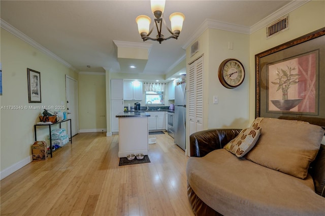 kitchen with stainless steel refrigerator, decorative light fixtures, sink, white cabinets, and light hardwood / wood-style flooring