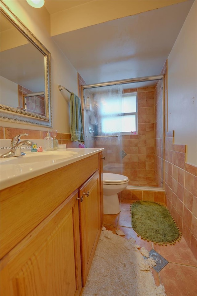 bathroom featuring tile walls, vanity, a shower with shower door, tile patterned floors, and toilet