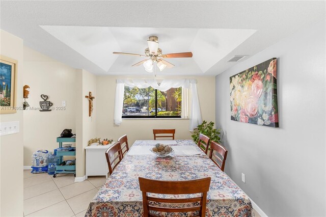 tiled dining area featuring a raised ceiling and ceiling fan