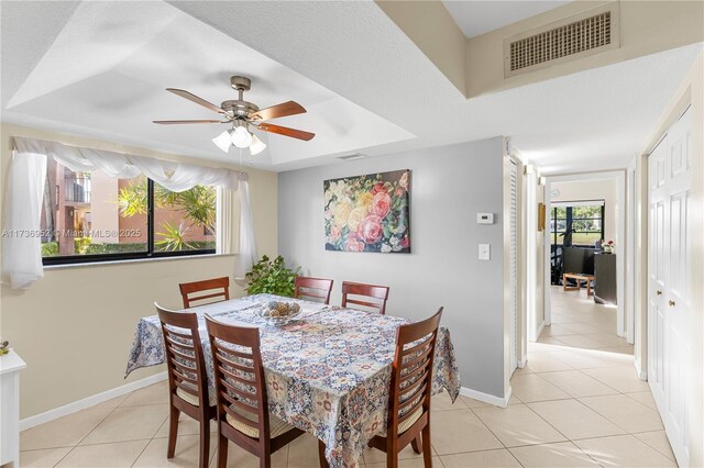 dining room with light tile patterned floors, a tray ceiling, and ceiling fan