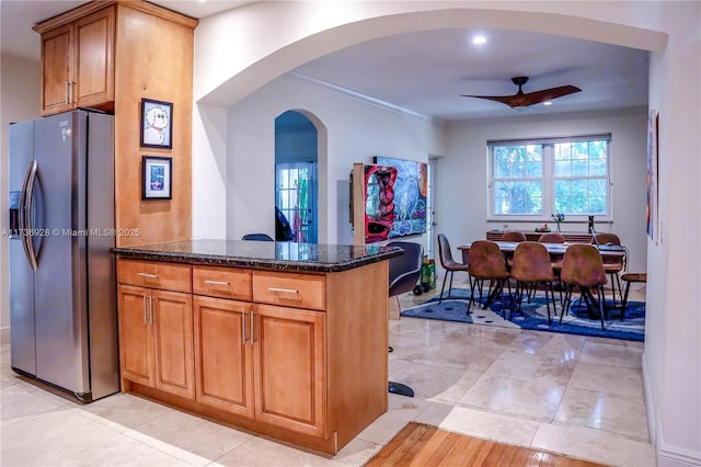 kitchen with light tile patterned floors, ceiling fan, dark stone countertops, stainless steel refrigerator with ice dispenser, and ornamental molding