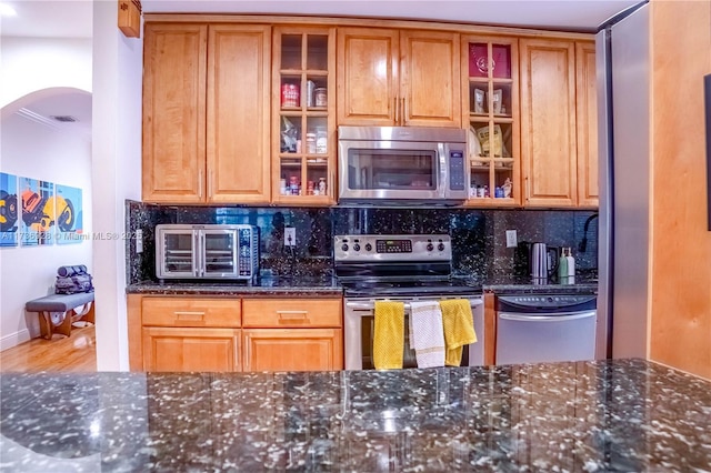 kitchen with tasteful backsplash, wood-type flooring, appliances with stainless steel finishes, and dark stone countertops