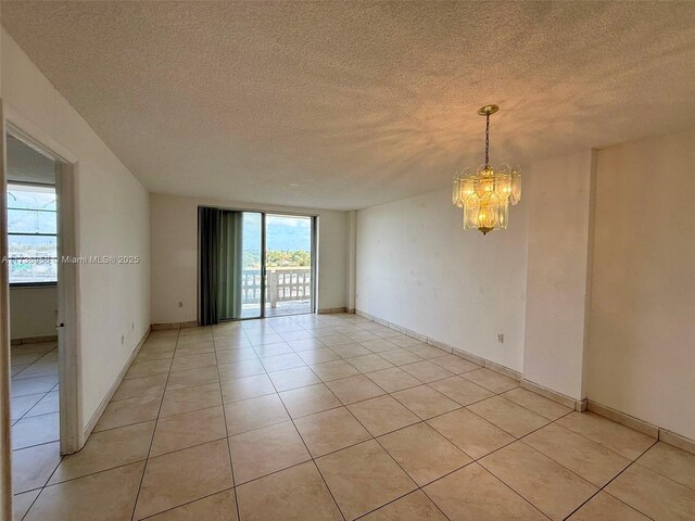 spare room with light tile patterned floors, a textured ceiling, and an inviting chandelier