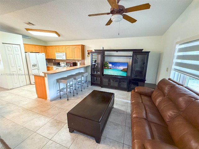 tiled living room with ceiling fan, vaulted ceiling, and a textured ceiling