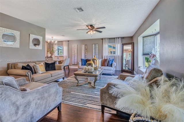 living room with ceiling fan with notable chandelier, dark hardwood / wood-style floors, and a textured ceiling