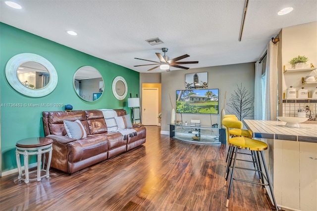 living room featuring a textured ceiling, dark wood-type flooring, and ceiling fan