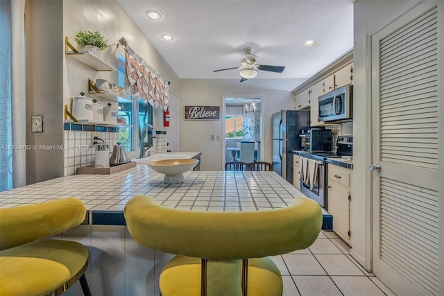 kitchen with sink, tile countertops, light tile patterned floors, appliances with stainless steel finishes, and ceiling fan