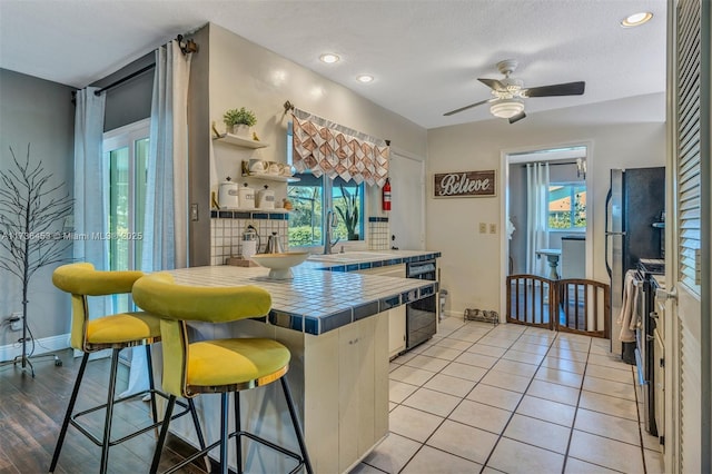 kitchen featuring sink, a breakfast bar area, stainless steel range with electric stovetop, tile counters, and dishwasher