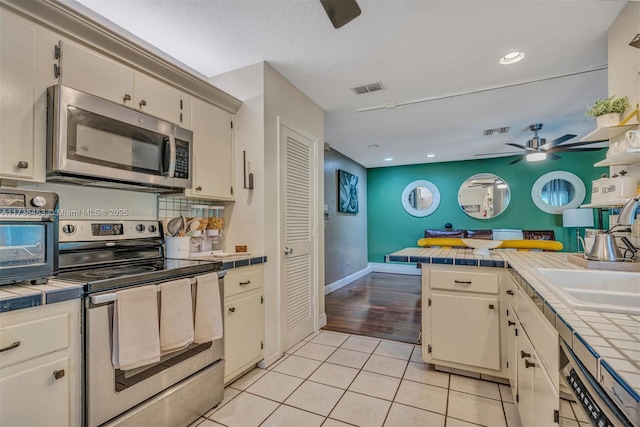 kitchen with light tile patterned flooring, sink, tile countertops, ceiling fan, and stainless steel appliances