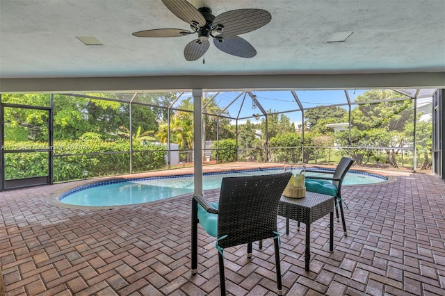 view of swimming pool with glass enclosure, ceiling fan, and a patio area