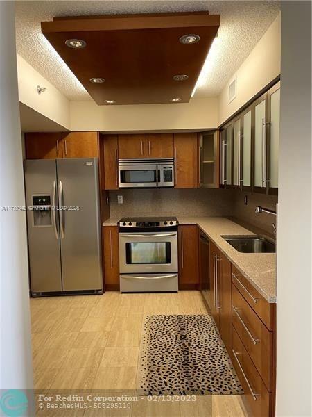 kitchen with sink, appliances with stainless steel finishes, backsplash, light stone countertops, and a textured ceiling