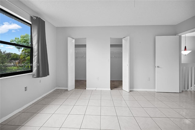 unfurnished bedroom with two closets, a textured ceiling, and light tile patterned floors