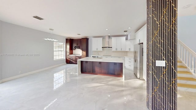 kitchen featuring stainless steel refrigerator, decorative light fixtures, sink, white cabinets, and wall chimney range hood