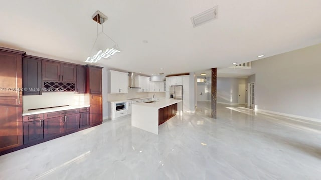 kitchen with stainless steel refrigerator with ice dispenser, white cabinetry, hanging light fixtures, an island with sink, and wall chimney range hood