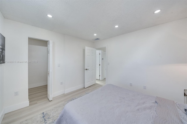 bedroom with a spacious closet, light hardwood / wood-style flooring, and a textured ceiling