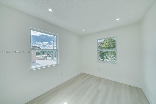 unfurnished room featuring light wood-type flooring, a textured ceiling, and a wealth of natural light