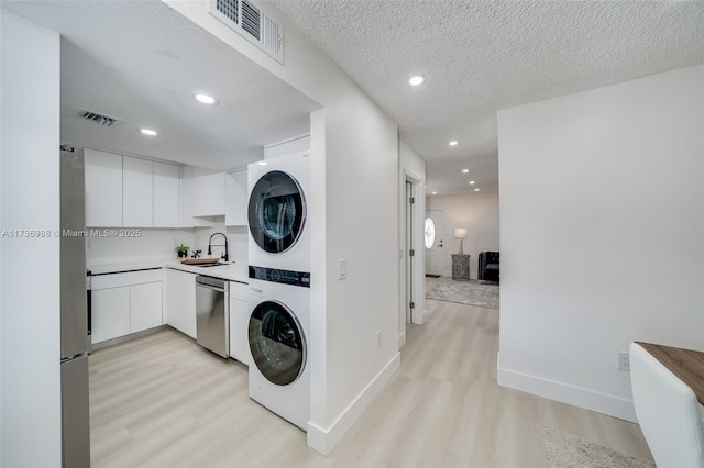 clothes washing area with sink, stacked washer / drying machine, a textured ceiling, and light wood-type flooring